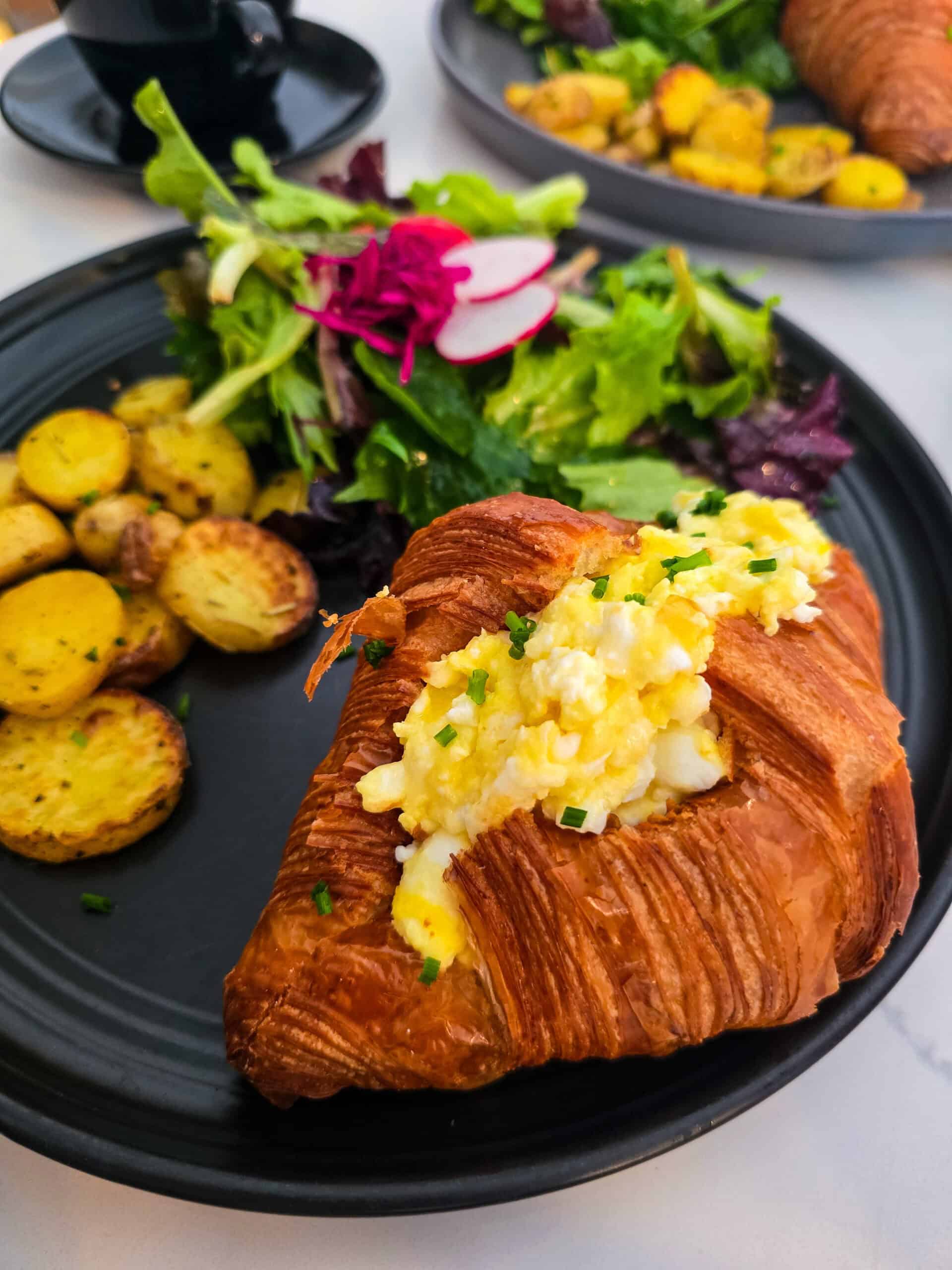 A croissant with eggs and potatoes on a plate at a cafe in Kensington Market, Toronto.