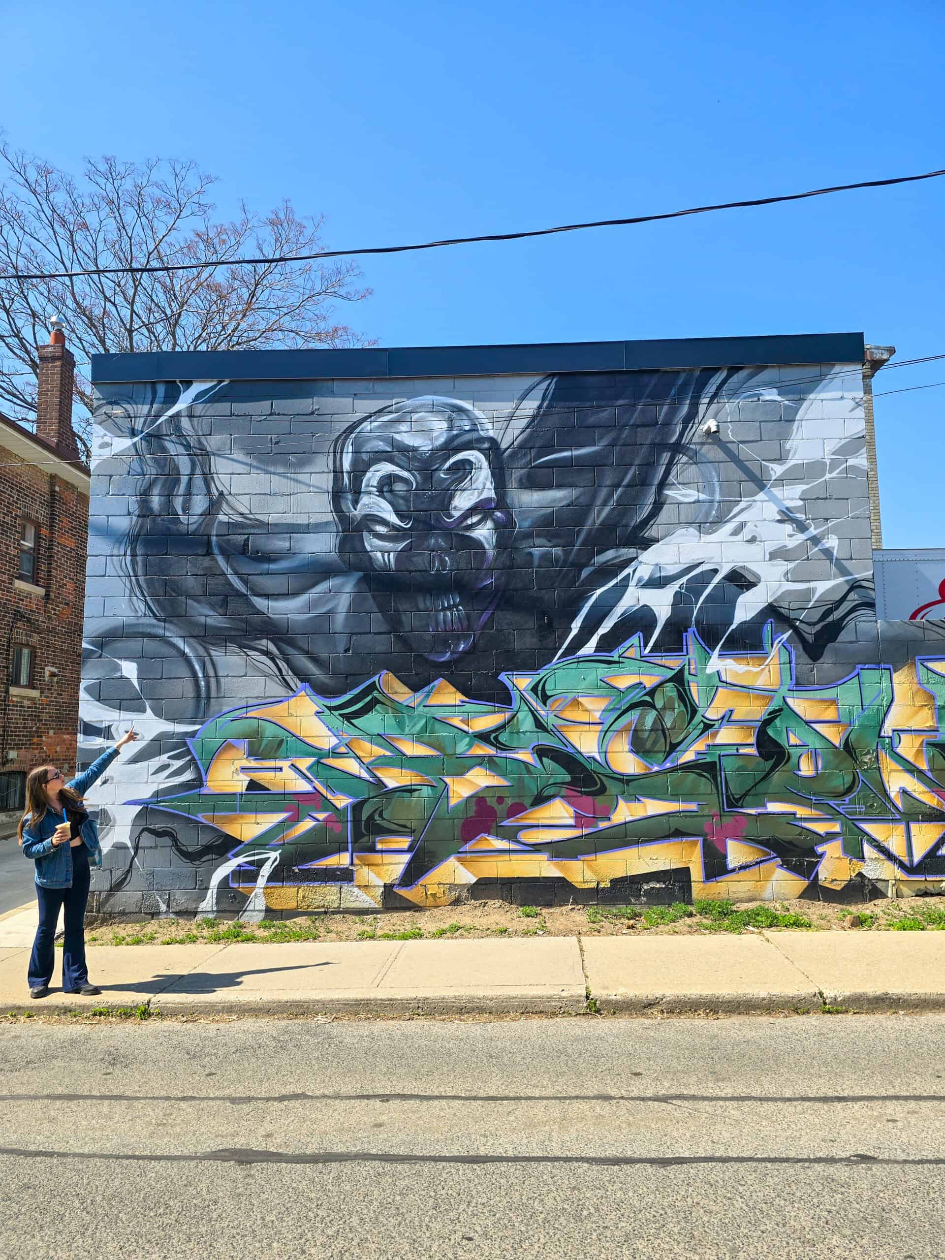 Tour guide Chloe stands in front of a large double mural pointing up as she explains techniques